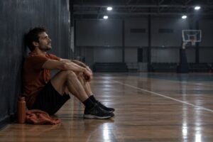 Atleta exausto sentado sozinho no chão da quadra, expressando burnout esportivo