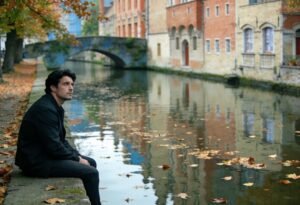O que é ressentimento: homem sentado sozinho à beira de um canal em cidade europeia no outono, olhando para cima, pensativo