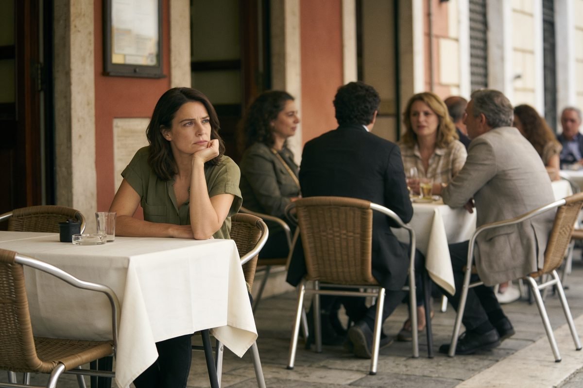 Solidão emocional: mulher sentada sozinha em uma mesa de café ao ar livre, cercada por outras pessoas conversando, representando a solidão emocional