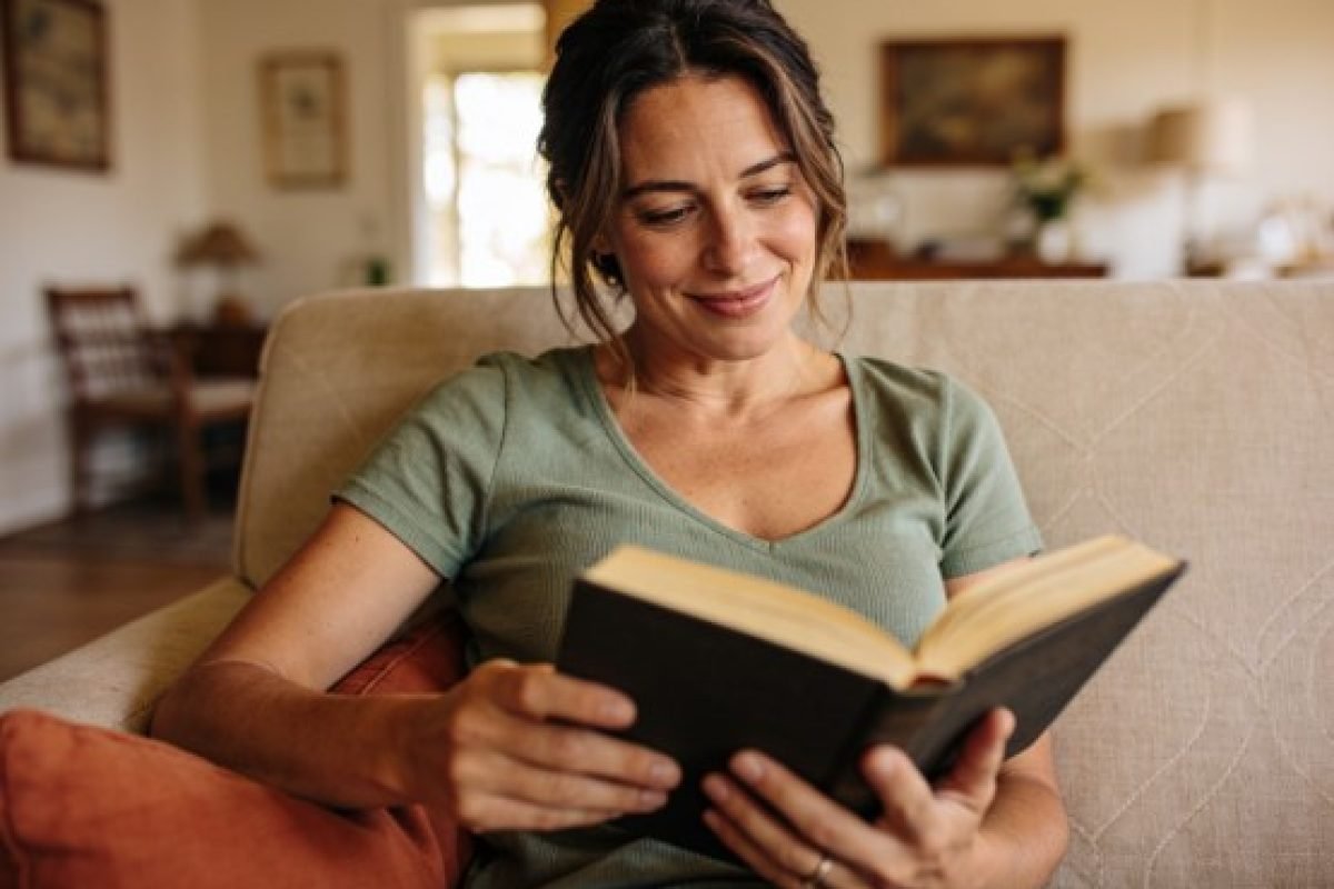 mulher sorrindo lendo um livro em casa, ilustrando o tema carência afetiva