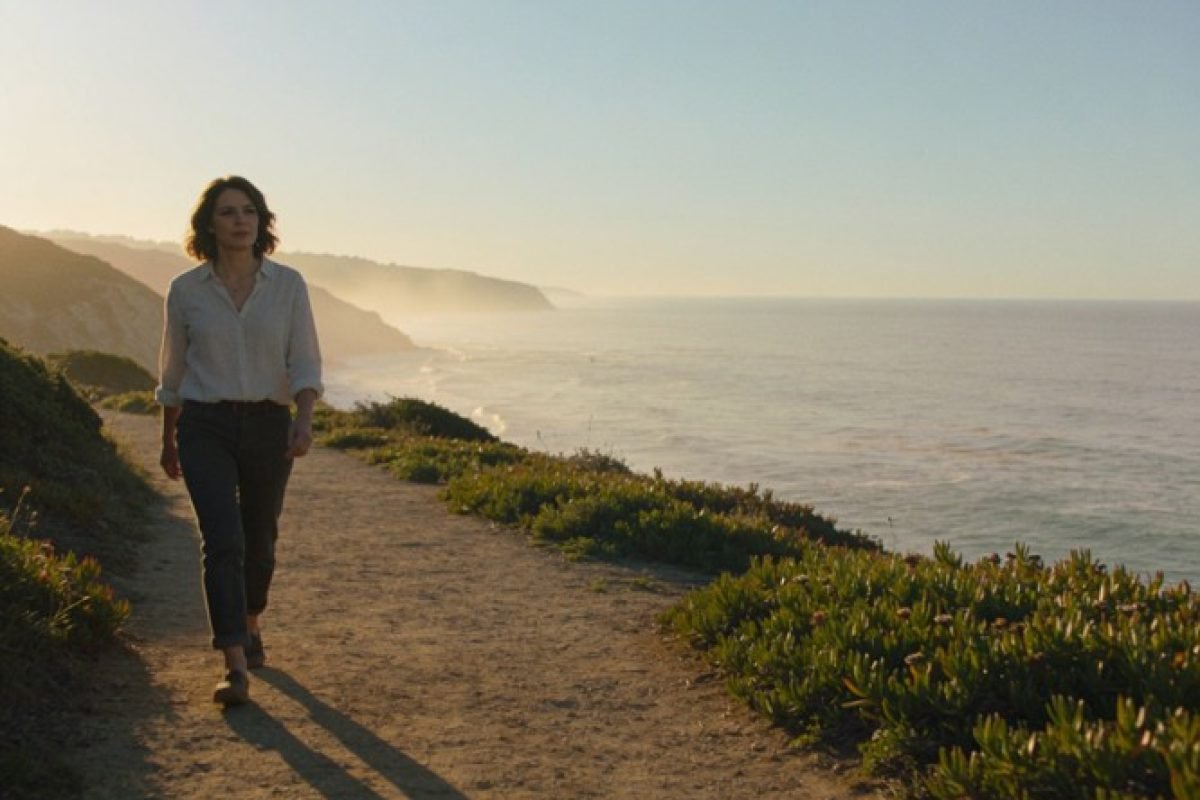 O que é esperança: mulher caminhando por uma trilha costeira ao entardecer, olhando para o horizonte